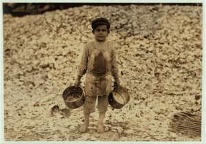 Manuel, the young shrimp-picker, five years old, and a mountain of child-labor oyster shells behind him. He worked last year. Understands not a word of English. Dunbar, Lopez, Dukate Company. Location: Biloxi, Mississippi. 1911 February. Hine, Lewis 1874-1940, photographer. (LC-DIG-nclc-00828). Library of Congress Prints and Photographs Division Washington, D.C.