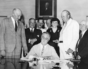 Roosevelt_Signs_the_Social_Security_Act Roosevelt signs into law the Social Security Act, one of Frances Perkins’s (standing behind Roosevelt) primary policy initiatives.