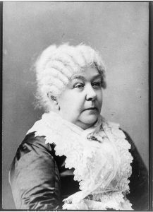 Photograph of Elizabeth Cady Stanton. Her white hair is curled and she wears lace over a dark dress. She is seated.