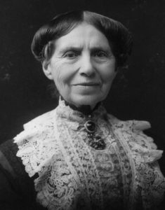 Photograph of Clara Barton smiling. She wears lace over her dark dress and a broach at her neck